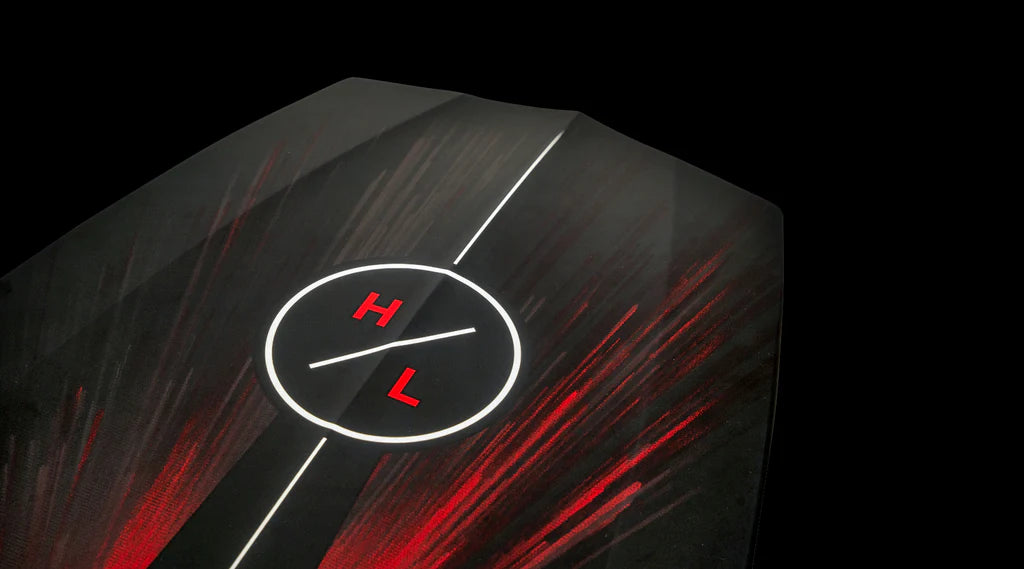 Close-up of the Hyperlite 2025 Time Machine Wakesurf Board: a dark board with red streaks and a white circle featuring the letters H and L at the center, set against a black background.