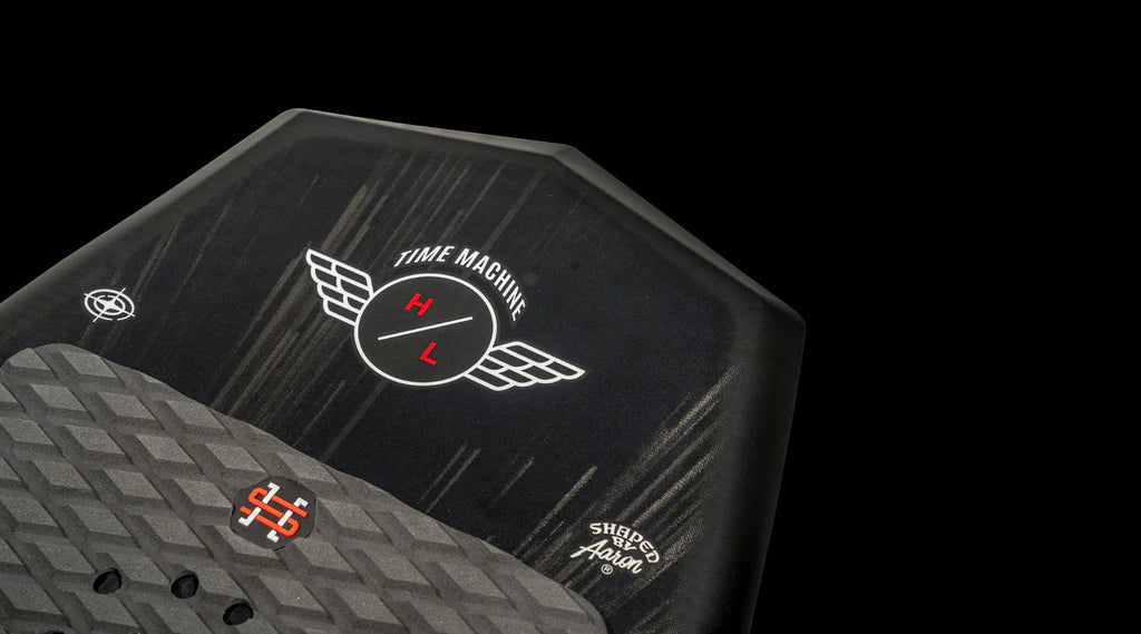 A close-up of the Hyperlite 2025 Time Machine Wakesurf Board, showcasing its black deck adorned with a Time Machine design featuring wings, and a sleek surf style shape ideal for those dreaming of wake surfing on asphalt.