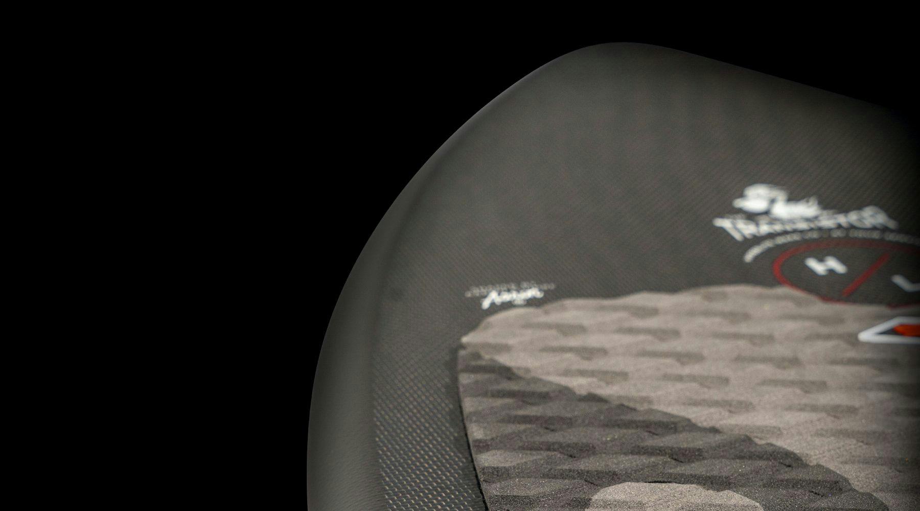 Close-up of a textured surface on a black object featuring a sleek woven carbon construction. The logo and lettering H L stand proudly on the right side against a dark background, exuding the precision typical of the Hyperlite 2025 Transistor Wakesurf Board design.