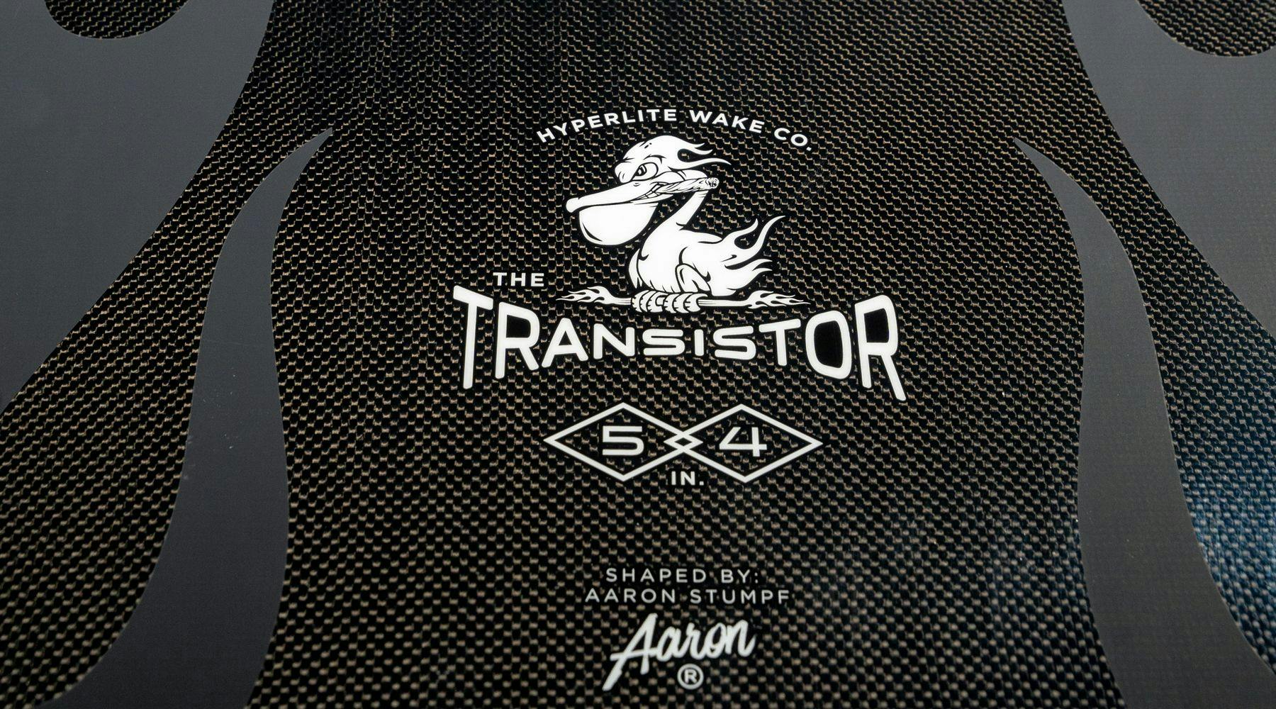 Close-up of a Hyperlite 2025 Transistor Wakesurf Board showcasing a cartoon duck logo and text: The Transistor, 54, designed by Aaron Stumpf. Featuring its Nova Core and woven carbon construction, this board guarantees an enhanced ride for wakesurfing enthusiasts.