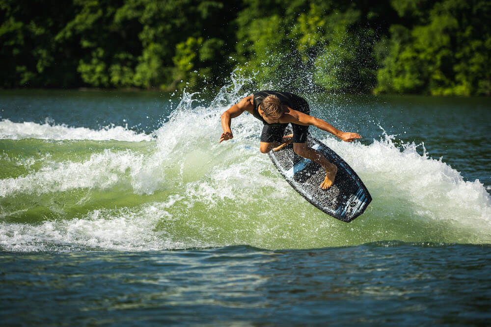 A man showcasing his surf style as he rides a wave on a Hyperlite 2024 Time Machine Wakesurf Board.