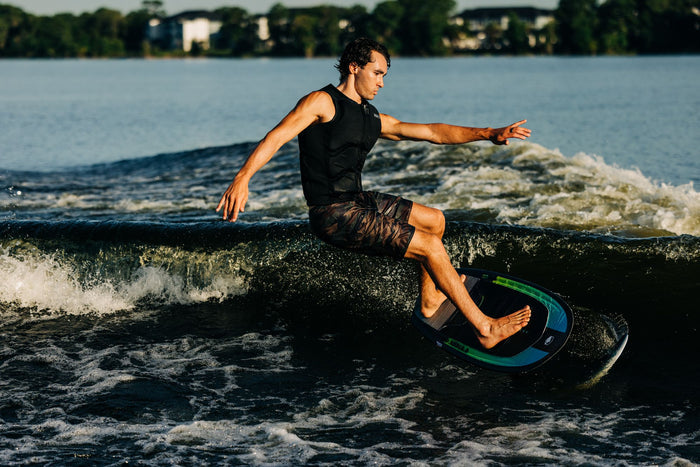 A man riding a wave on a wakeboard. The construction of the Liquid Force 2024 Nebula | Carbon Horizon Surf 120 Foil Package ensures stability and control as he gracefully foils through the water.