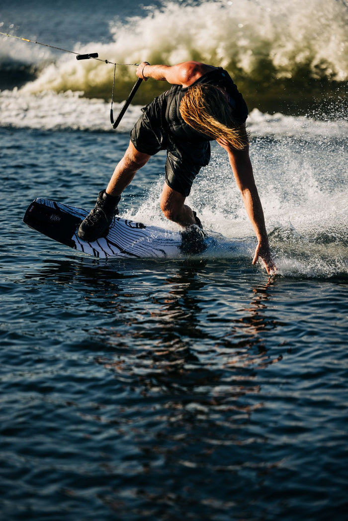 A person riding a Liquid Force 2024 RDX wakeboard in the water.