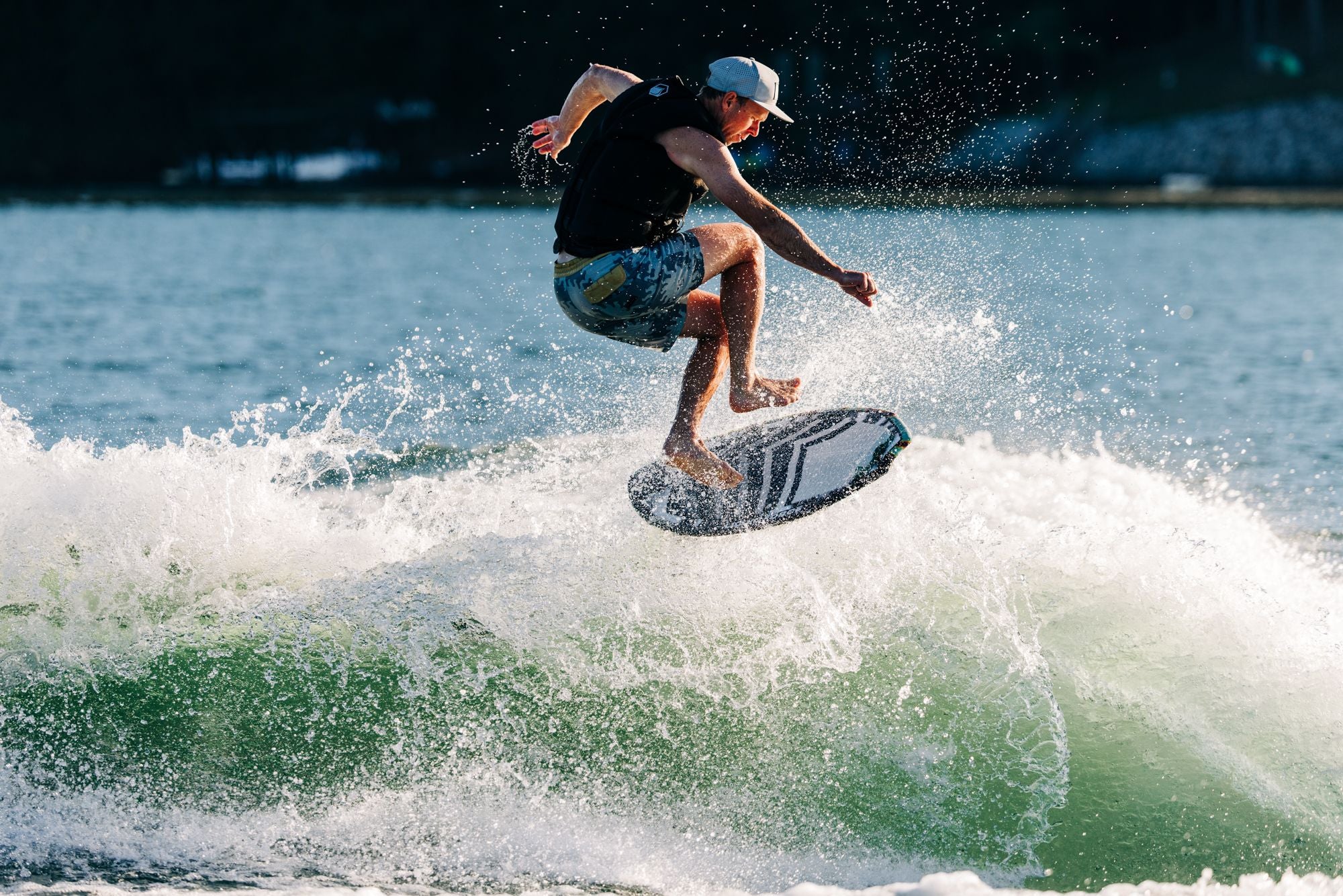 Wearing a cap and shorts, an individual showcases professional-level talent by executing a high-flying jump on the Liquid Force 2025 Ace Wakesurf Board, effortlessly skimming over the wave in this agile wakesurfing performance.