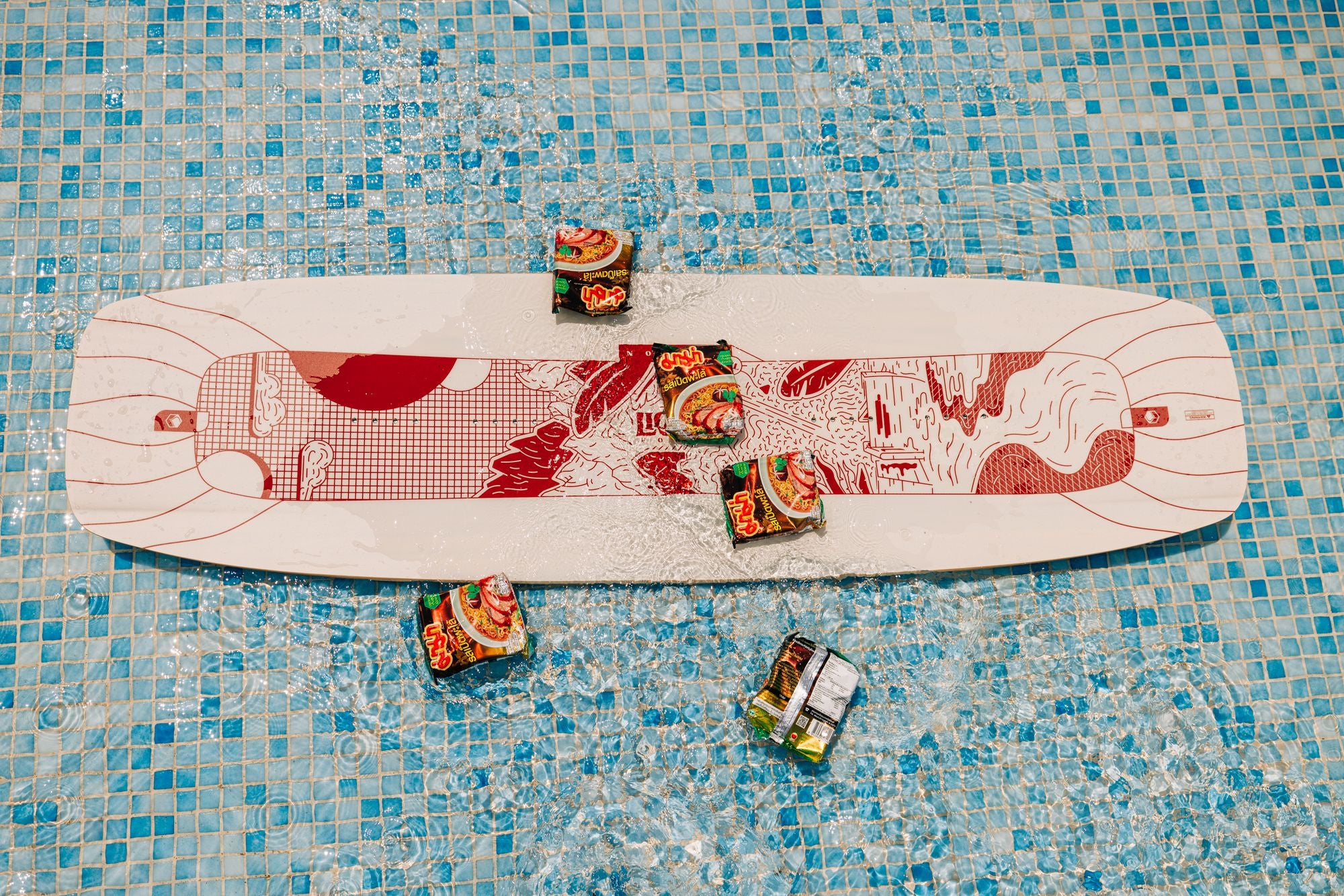 A Liquid Force 2025 Noodle Wakeboard featuring a red and white design floats in a pool, accompanied by five packets of instant noodles. The scene embodies the perfect fusion of flex and chill vibes, as if the lines between wakeboarding and lounging in sunny serenity have seamlessly blended.