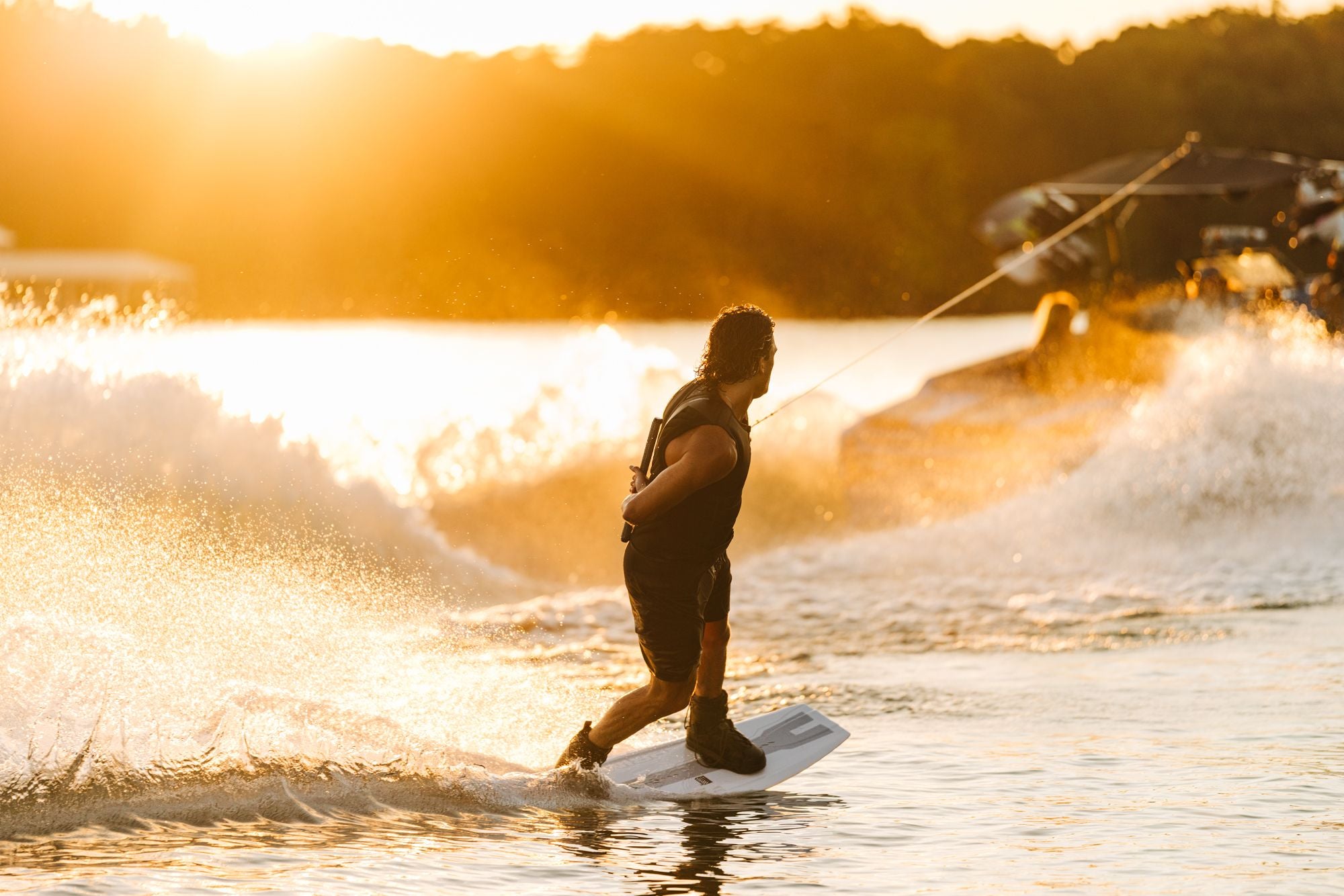 A person wakeboarding on a sunlit lake, being pulled by a motorboat creating splashes, showcases the agility of the Liquid Force 2025 Prime Aero Wakeboard. As the waves rise, you can almost see Fynn Bullock grinning with exhilaration on his wakeboard—an embodiment of pure aquatic adventure.