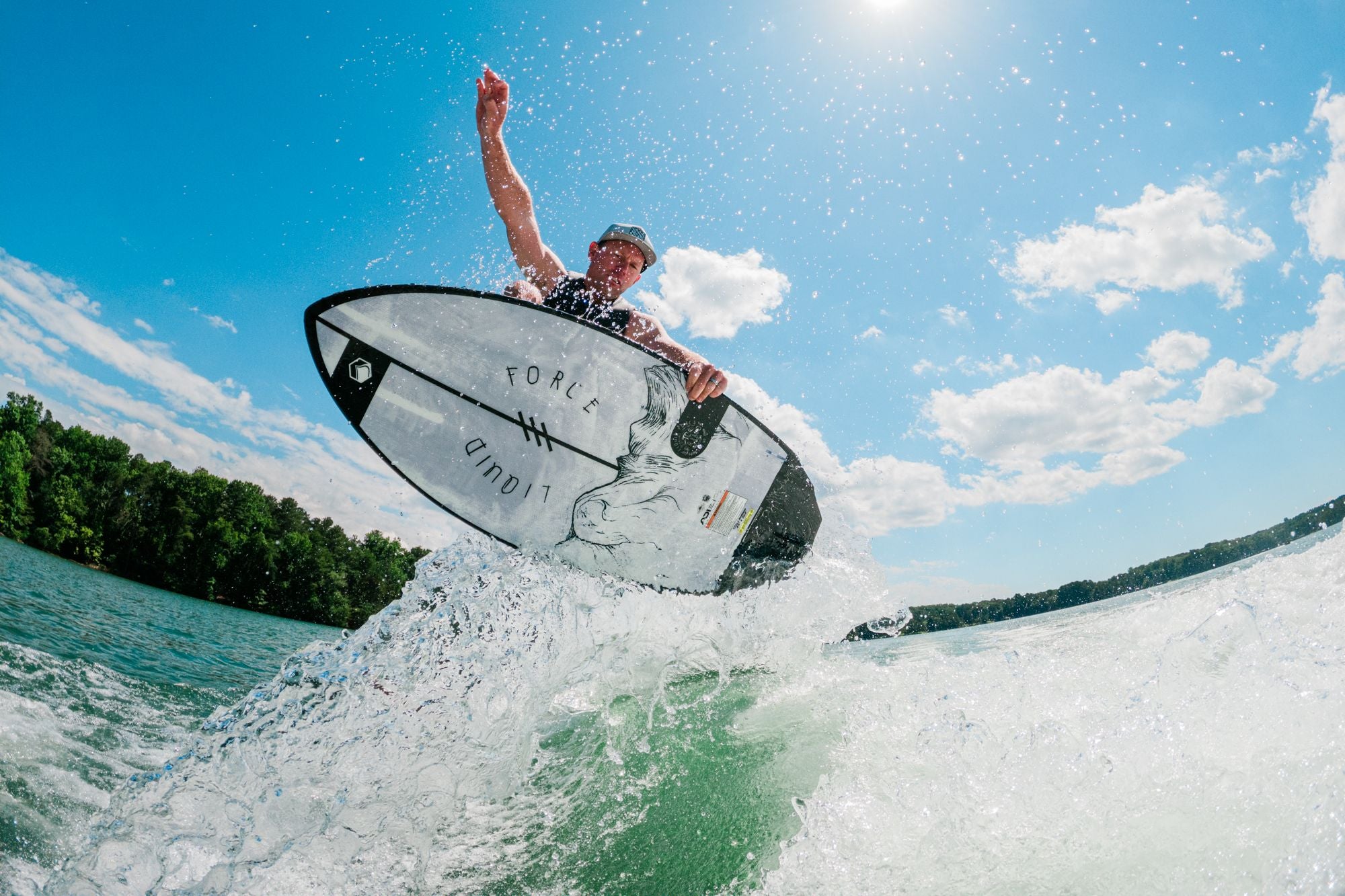 A person surfing on a wave with the Liquid Force 2025 Primo Wakesurf Board, reaching upward, under a clear blue sky.