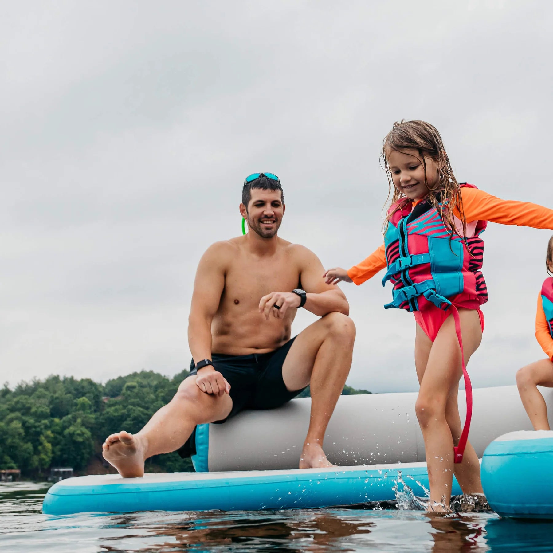 Little girl ventures into the water stepping off the MISSION Reef Lite Lounge Inflatable Water Mat (6.5' x11.5' x 6') while her Dad smiles in observation