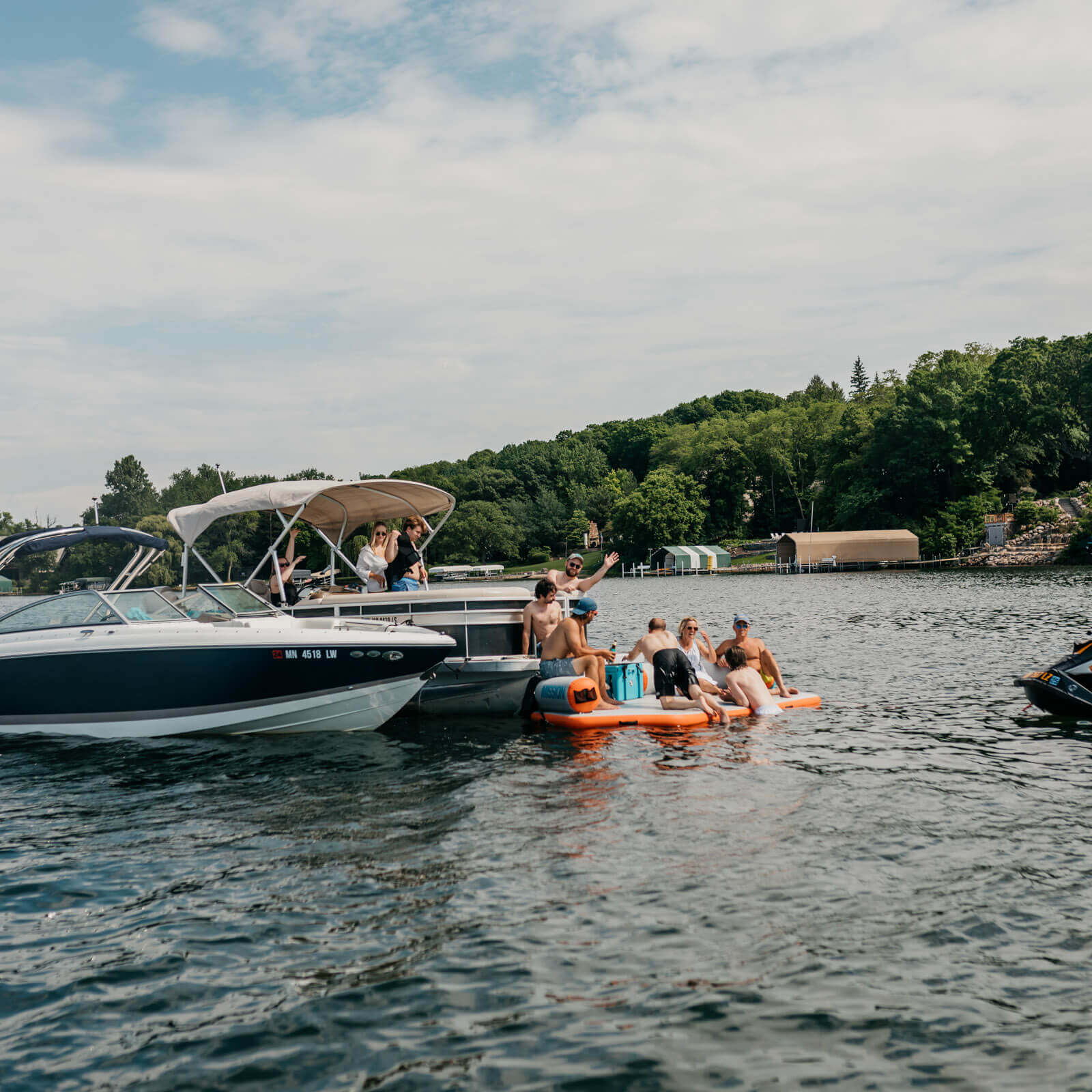 A group of people enjoying their time on a pontoon boat on a lake, equipped with a MISSION Reef Deck | Inflatable Swim Platform + Lounger for added fun and safety. They have also brought along various boat accessories including a MISSION.