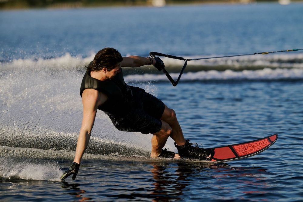 A person in black gear and gloves expertly carves across the lake on a sunny day, generating a huge spray as they showcase their skills with the Radar Session Waterski | Prime + ARTP 2026 from Radar.
