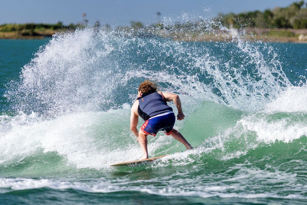 A person expertly skimming across a wave on a sunny day with the Ronix 2025 Element Core Blunt Nose Skimmer, its lightweight design from Ronix ensuring remarkable stability as they carve through the ocean, creating an impressive splash.