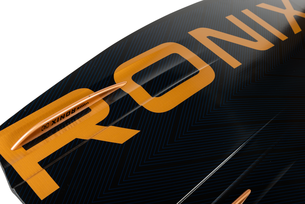 A close-up of a Ronix 2025 One Blackout Wakeboard, highlighting the brand logo and fin against a dark blue surface with orange accents.