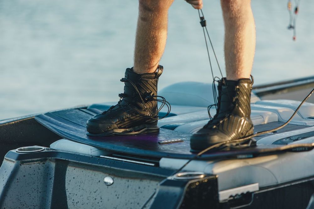 Close-up of a person wakeboarding in Ronix One Gloss Midnight Boots 2026, holding a tow rope while being pulled by a boat over the water.