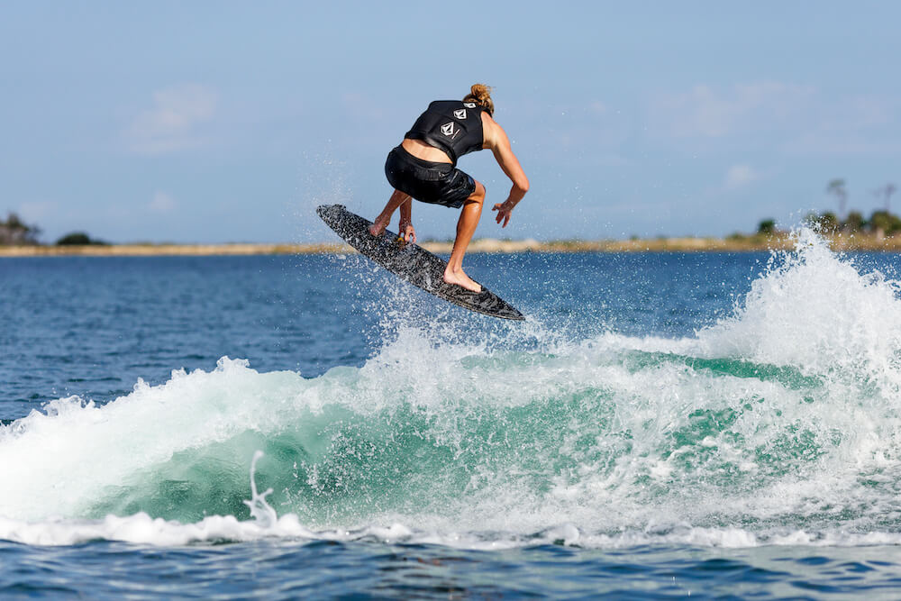 A person is riding a Ronix 2024 Beaux Skimmer Wakesurf Board on a lightweight surfboard.