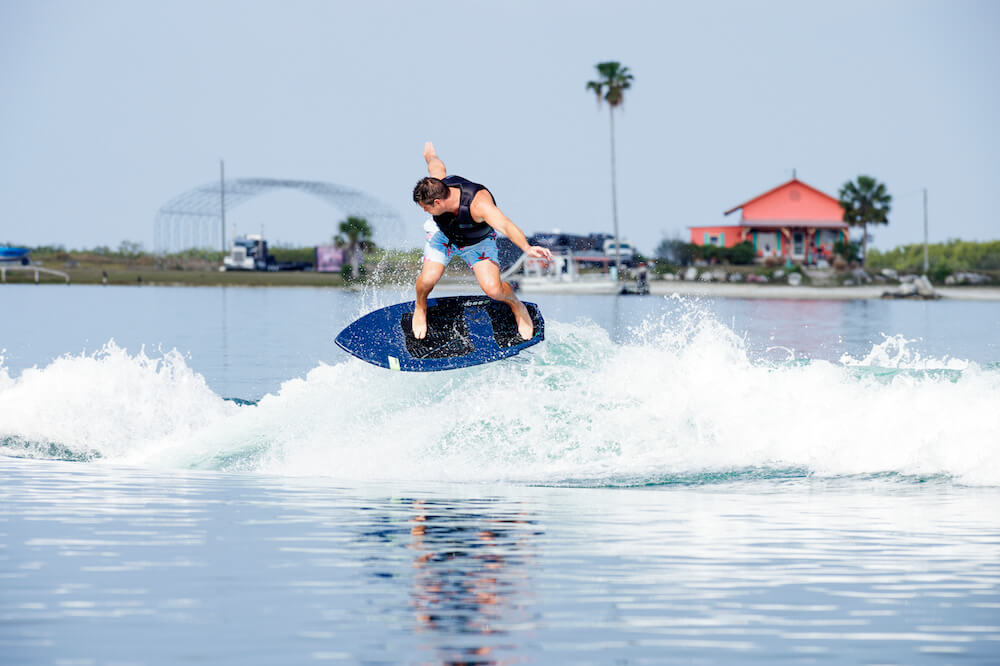 A man riding a wave on a Ronix 2024 H.O.M.E. Carbon Pro M50 Wakesurf Board with a button fin system.