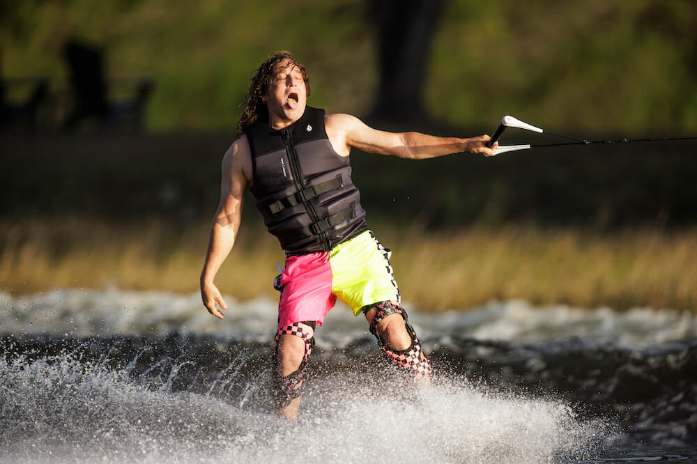 A man with a longer torso is water skiing using an eco-friendly Ronix Volcom YES Men's CGA Vest made of sustainable materials.