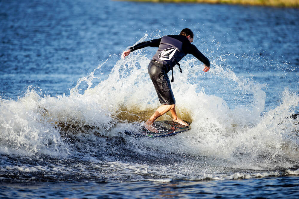 A man riding a wave on a Ronix surfboard made of eco-friendly materials.