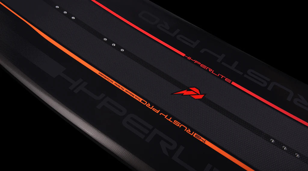 A black and orange surfboard in the shape of a Hyperlite 2024 Rusty Pro wakeboard, set against a black background.