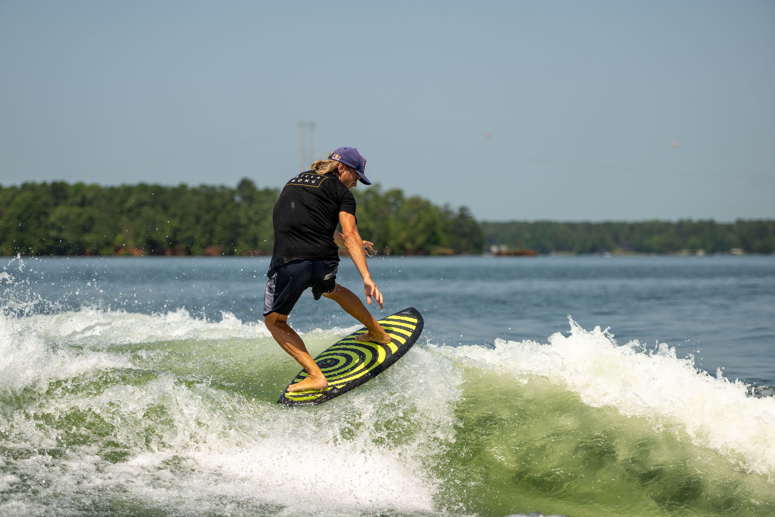 A Hyperlite 2024 Shim wakesurf enthusiast effortlessly rides a wave on a surfboard constructed with DuraShell technology.