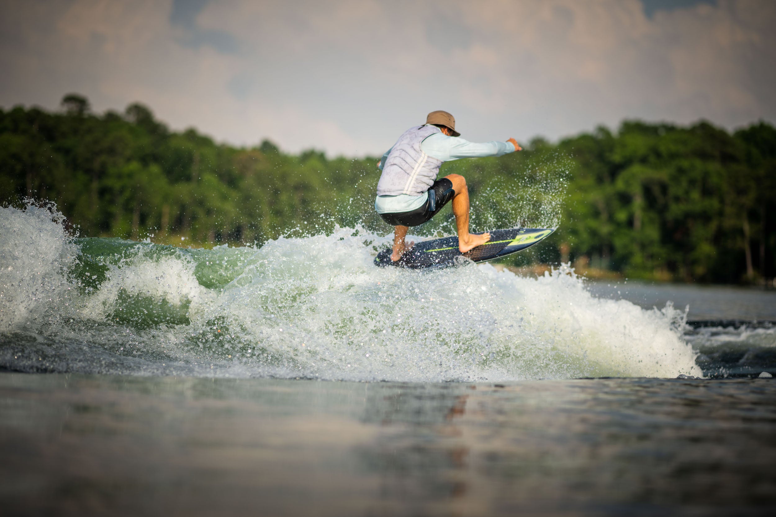 A man is riding a wave on a surfboard, showcasing the Hyperlite 2023 Buzz Wakesurf Board and its DuraShell construction.