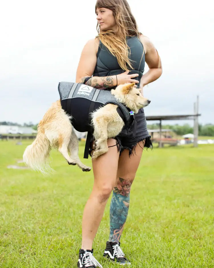 A woman with tattoos holding a dog in a Follow Dog Floating Aid - Black harness with buckle straps made by Follow Wake.