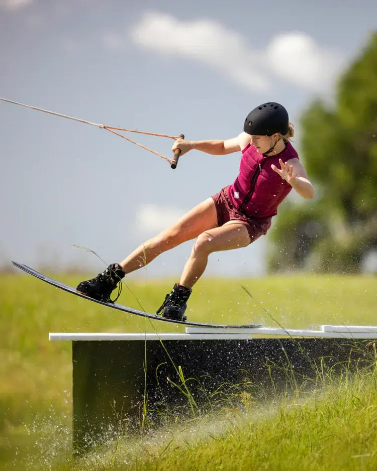 A girl is performing a trick on a water ski while wearing a Follow Cord Ladies Jacket - Maroon by Follow Wake.