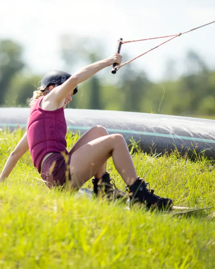 A woman is kiteboarding in a grassy field, wearing a Follow Cord Ladies Jacket - Maroon and benefiting from the TrueFit© Liner.