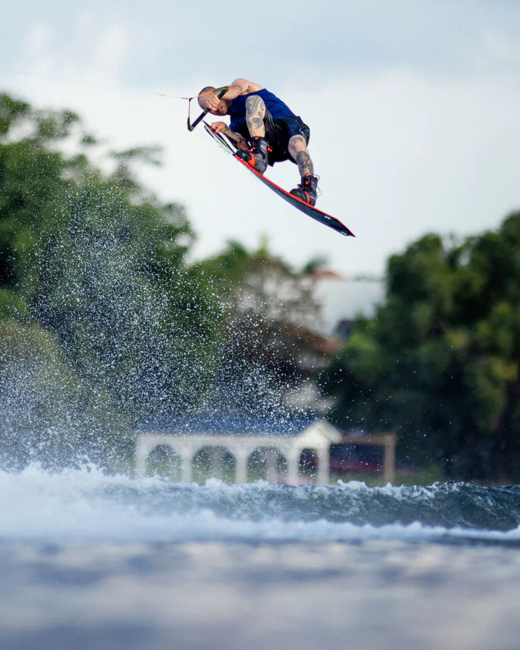 A man is riding a Follow Wake 2022 BP Pro Men's Jacket - Navy wake board in the air, enjoying comfortable and thrilling moments while being protected by impact protection technology.