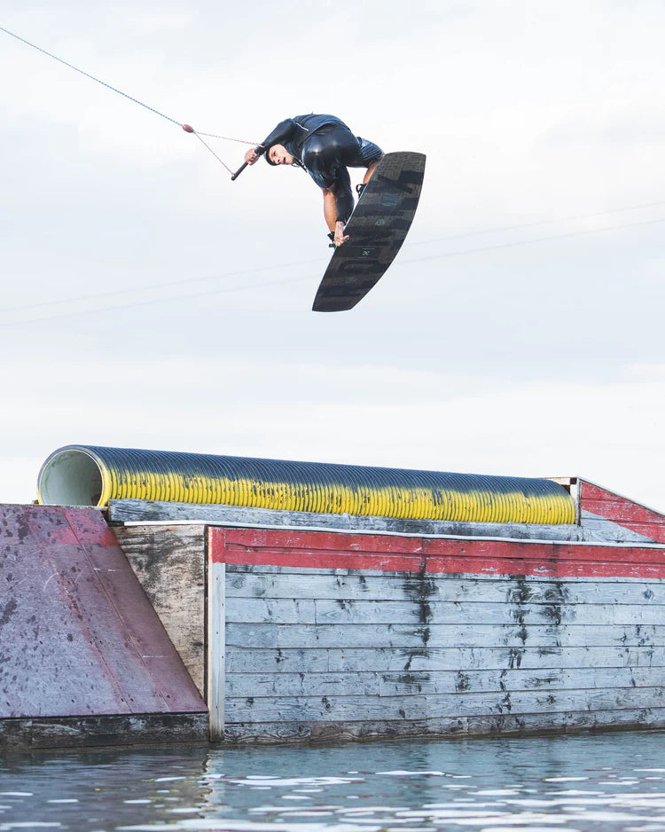 A man is expertly riding a Follow Wake wakeboard in the water, showcasing his impressive skills and precision control.