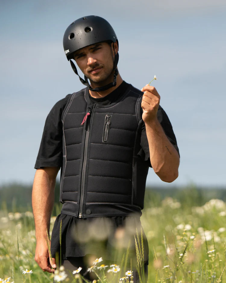 A man wearing a Follow 2022 TBA Men's Jacket - Black by Follow Wake in a field of flowers.