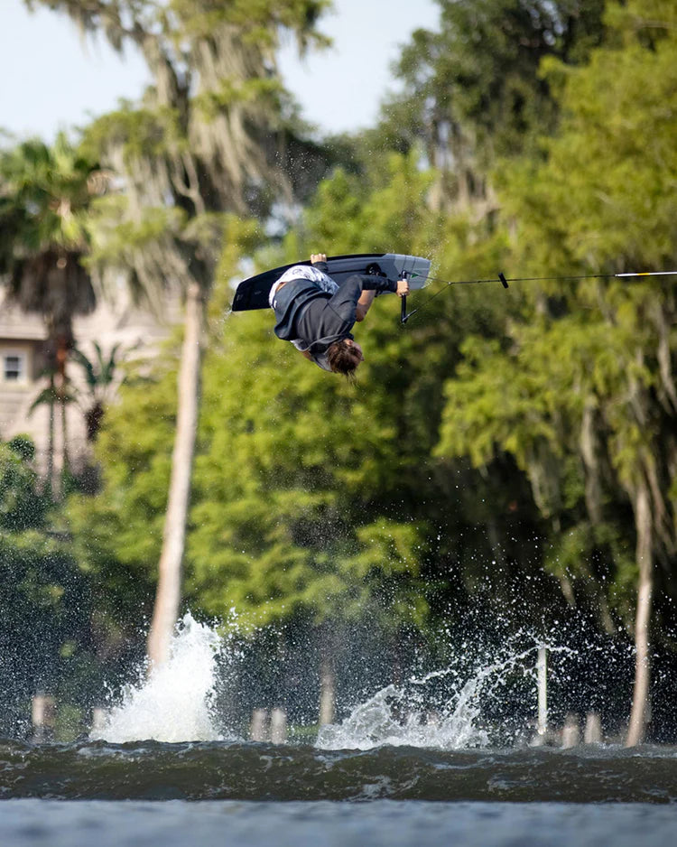 A man is doing an impressive trick on a wake board, braving the wind chill factor while wearing a Follow Wake neoprene jacket with Aquaguard® Stash pockets. The jacket is the Follow 3.12 Anorak Pro Neo Outer Jacket in Charcoal.