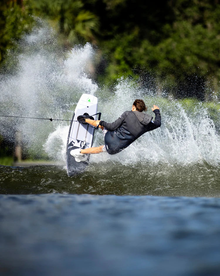 A man wakeboarding in the water, wearing a Follow Wake neoprene jacket to protect against the wind chill factor. The jacket is called the Follow 3.12 Anorak Pro Neo Outer Jacket - Charcoal.