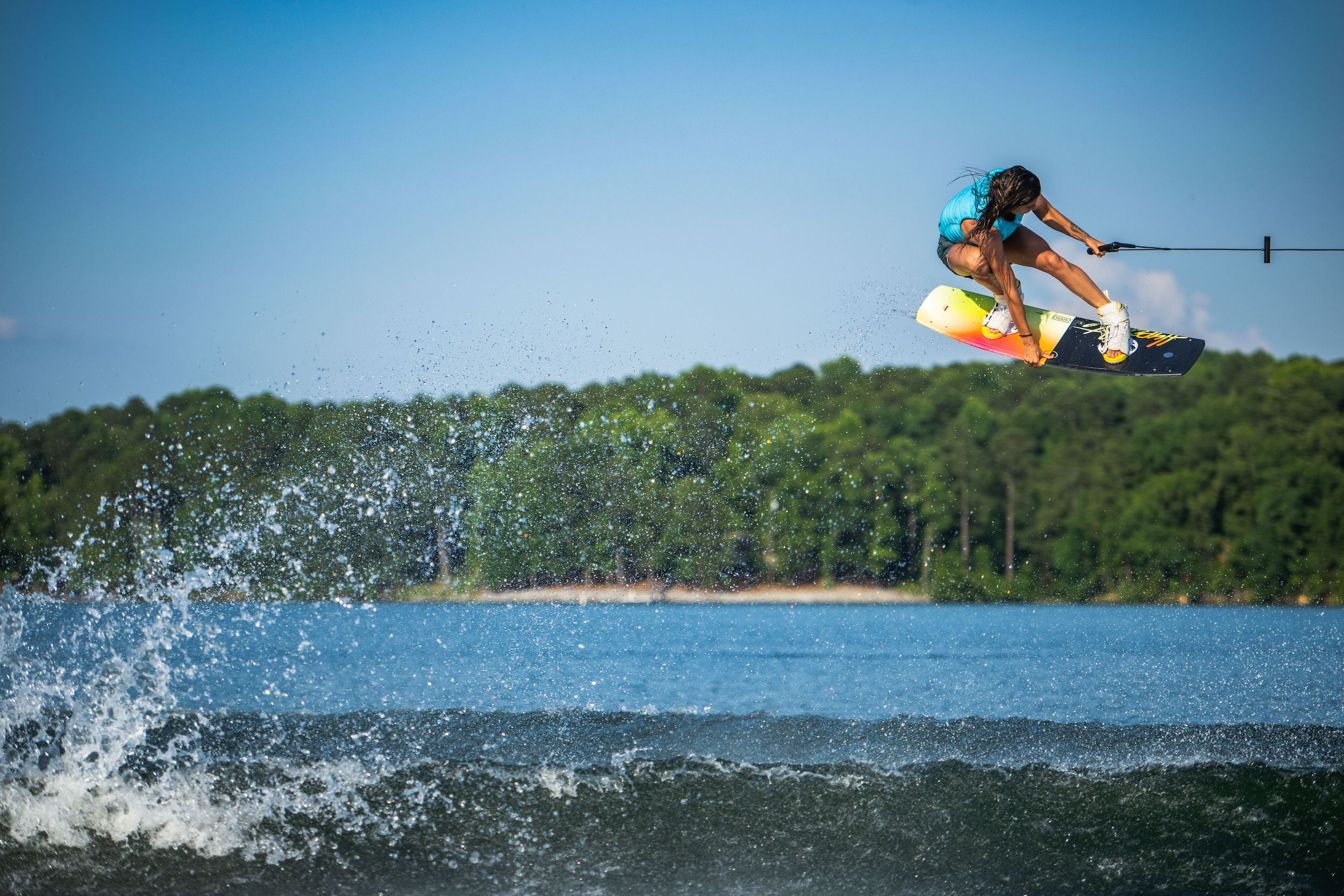 A woman is riding a wakeboard in the water, showcasing the Hyperlite 2023 Cadence Wakeboard from Hyperlite's Cadence series with Satin Flex technology.