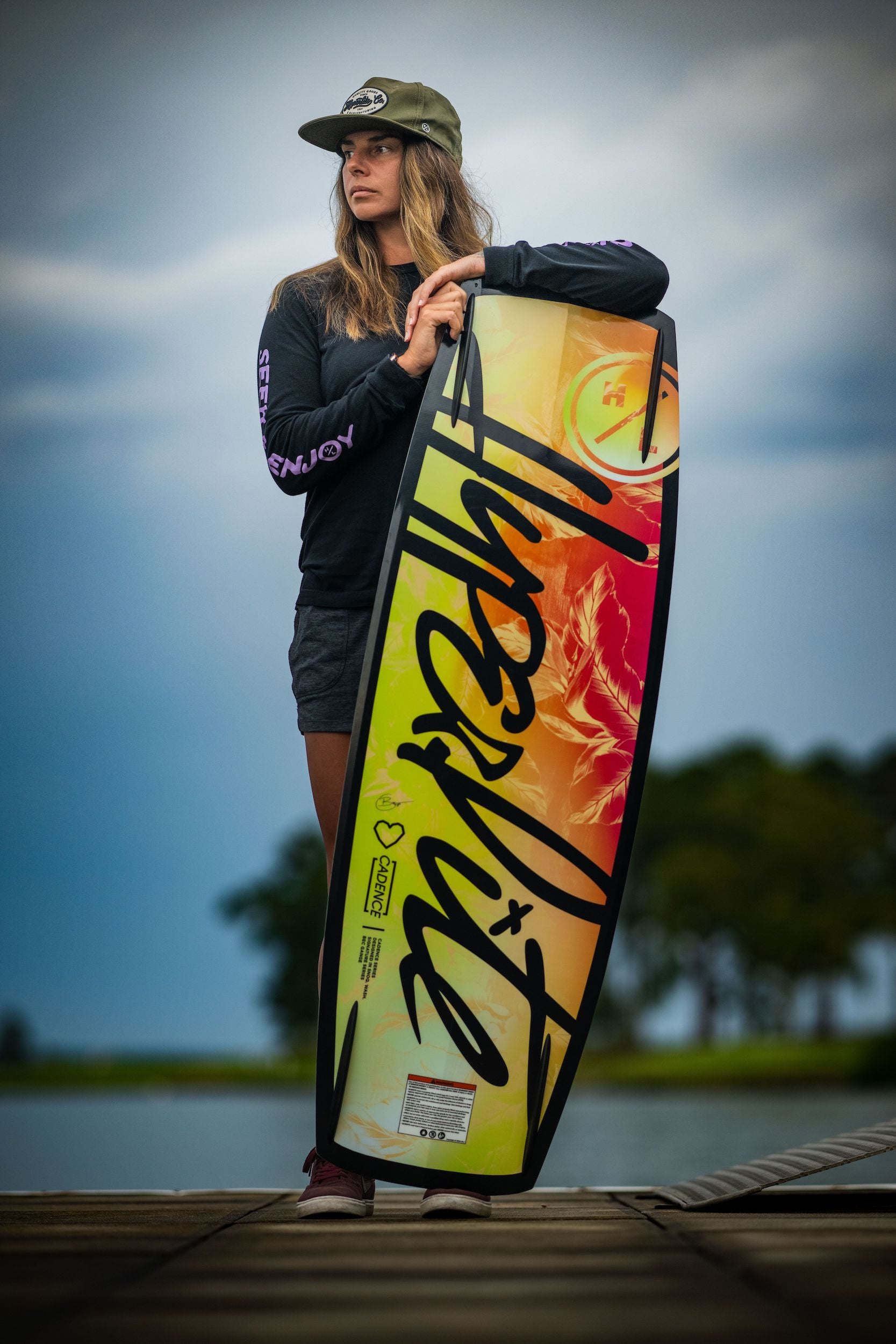 A woman holding a Hyperlite 2023 Cadence Wakeboard on a dock.