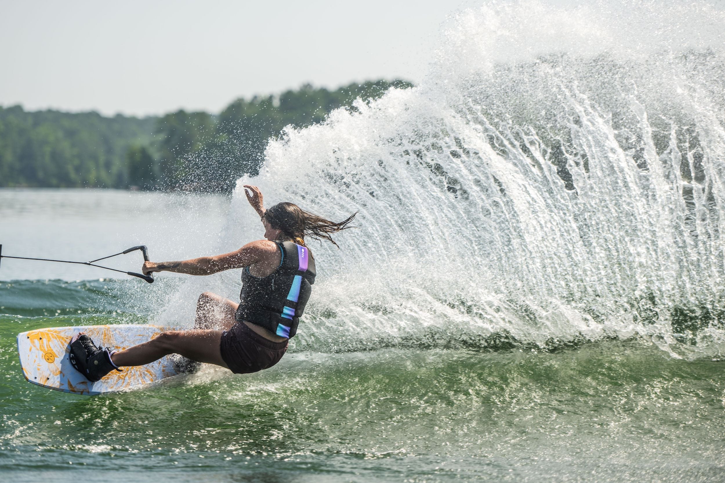 A Hyperlite 2023 Prizm Wakeboard inspired woman glides across the lake on her ladies wakeboard.