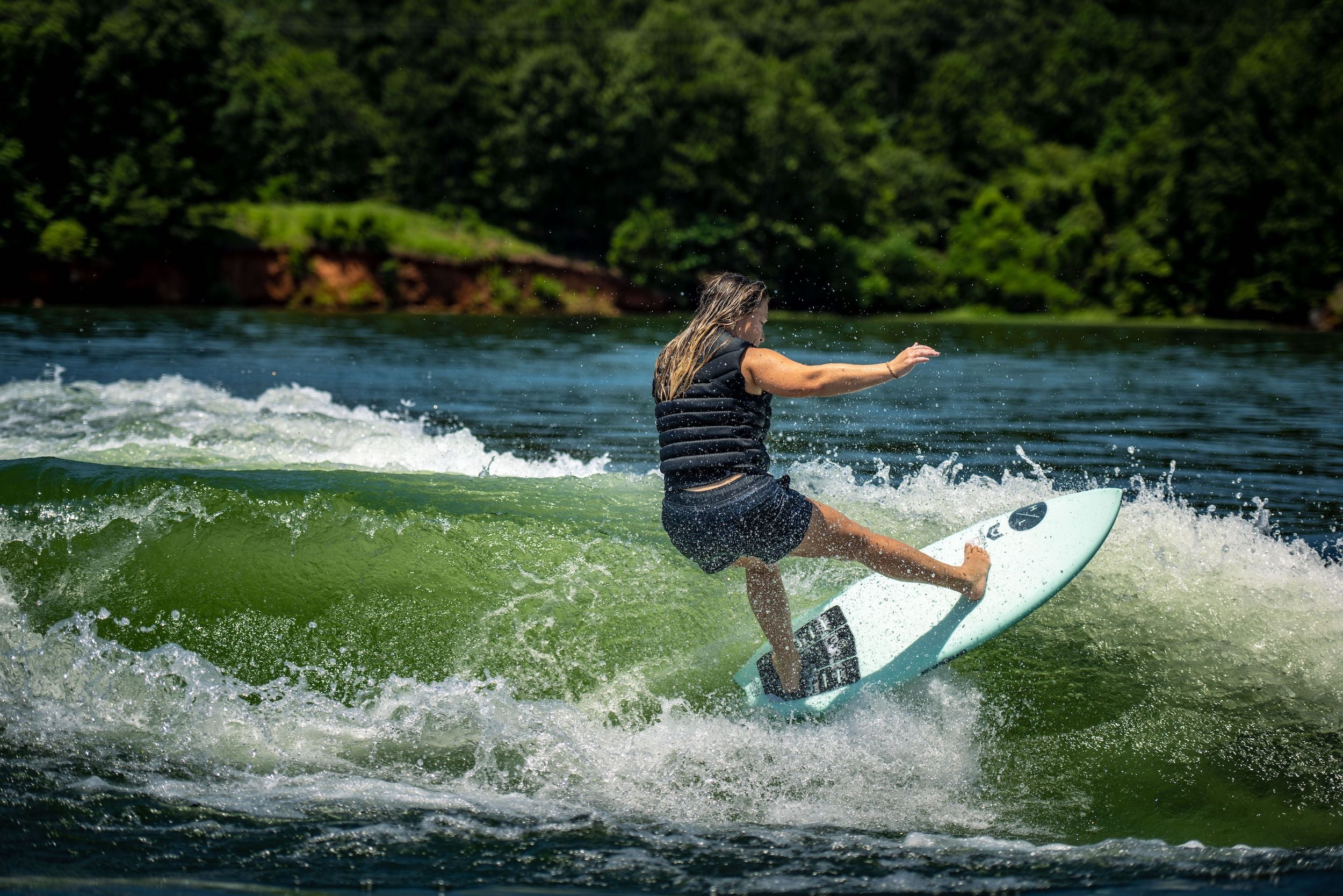 A woman riding a wave on a Hyperlite 2024 Varial Accelerator Wakesurf Board equipped with Varial Surf Technology.