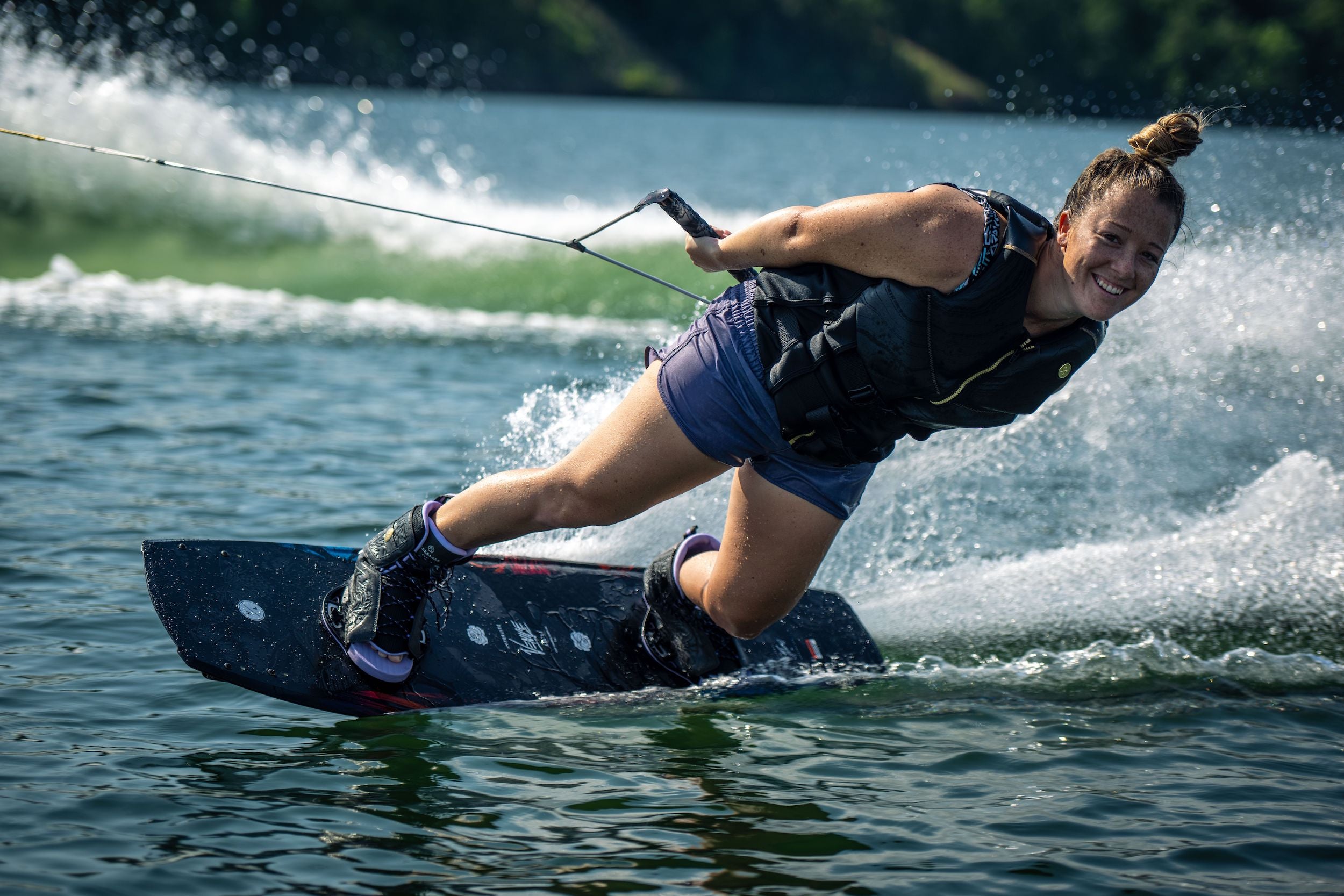 A woman wakeboarding on a lake with a Hyperlite 2023 Venice Wakeboard.