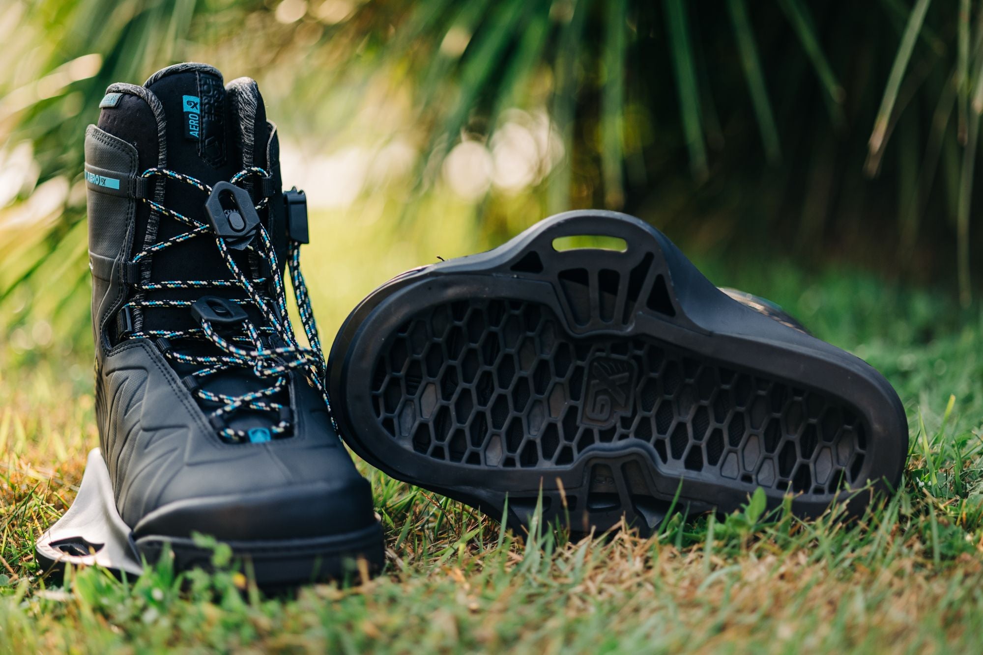 A pair of Liquid Force 2024 Aero 6X Boots - Black with a flexible support structure sitting on the grass.
