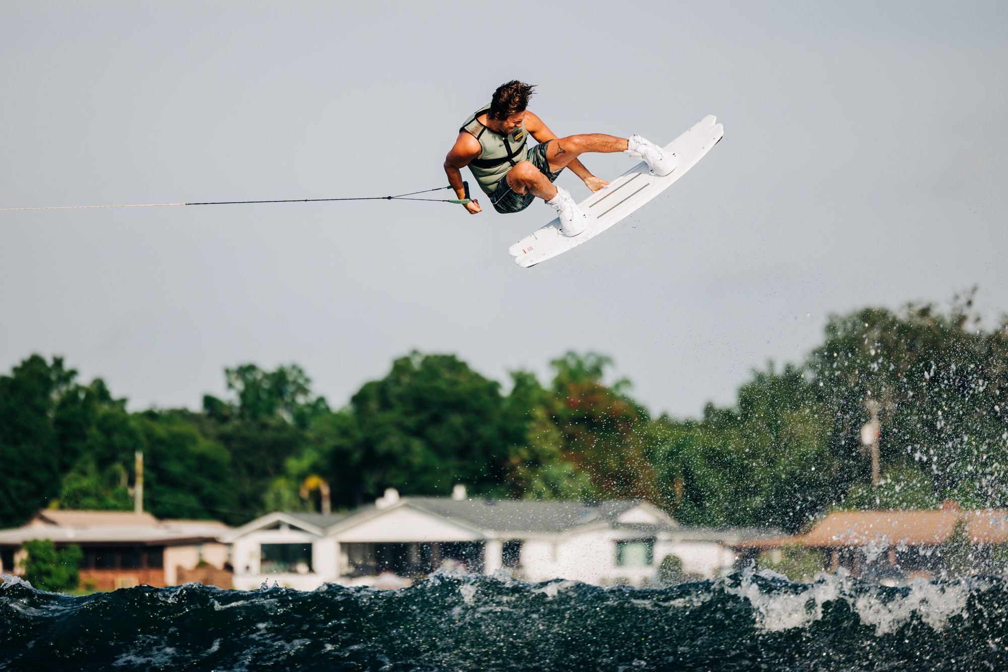 A woman wakeboarding in the air over a lake, showcasing her Liquid Force 2024 Aero 6X Boots - White bindings and flexible yet ultra-supportive experience.