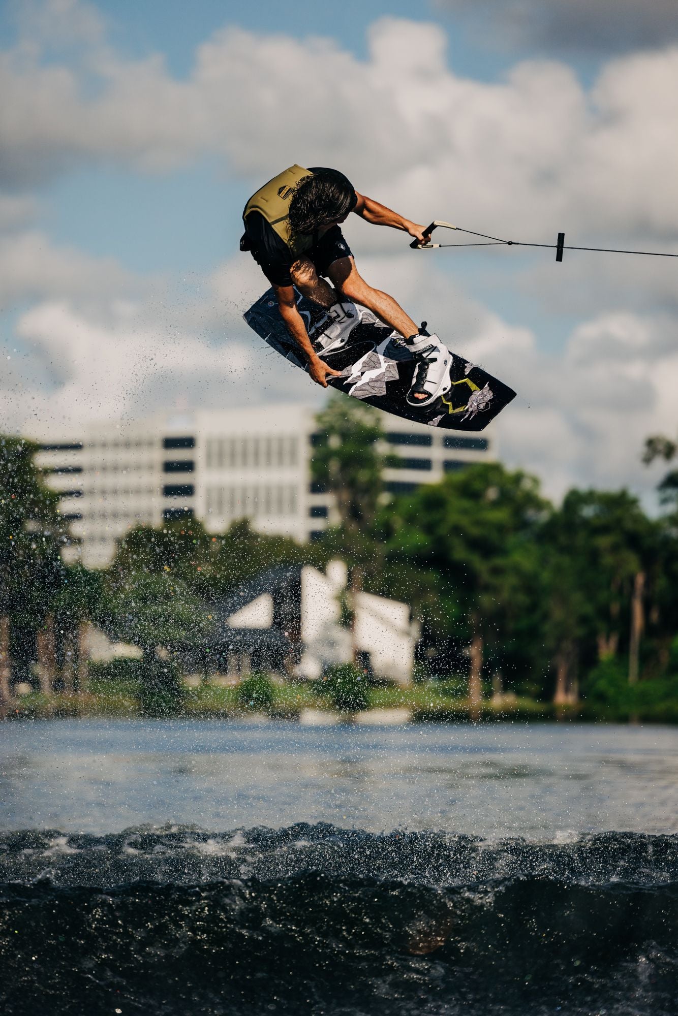 A person performing Liquid Force wakeboarding tricks in the air over a lake, showcasing explosive pop off the top and aggressive edge control.