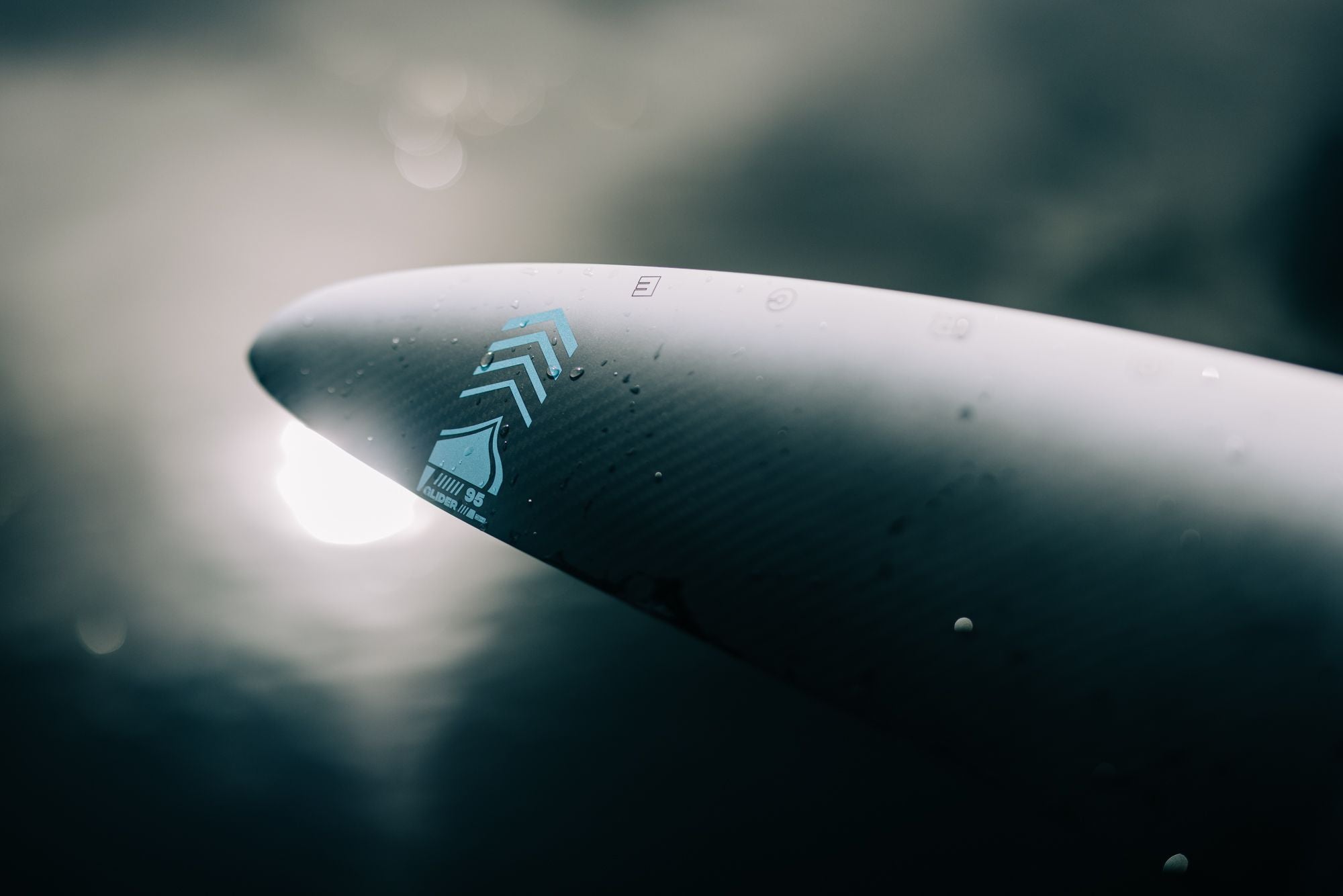 A close up of a Liquid Force 2024 Glider H.A. 95 Front Wing surfboard gliding on the water, enhanced by boat wakes and constructed with carbon fibre for optimal performance.