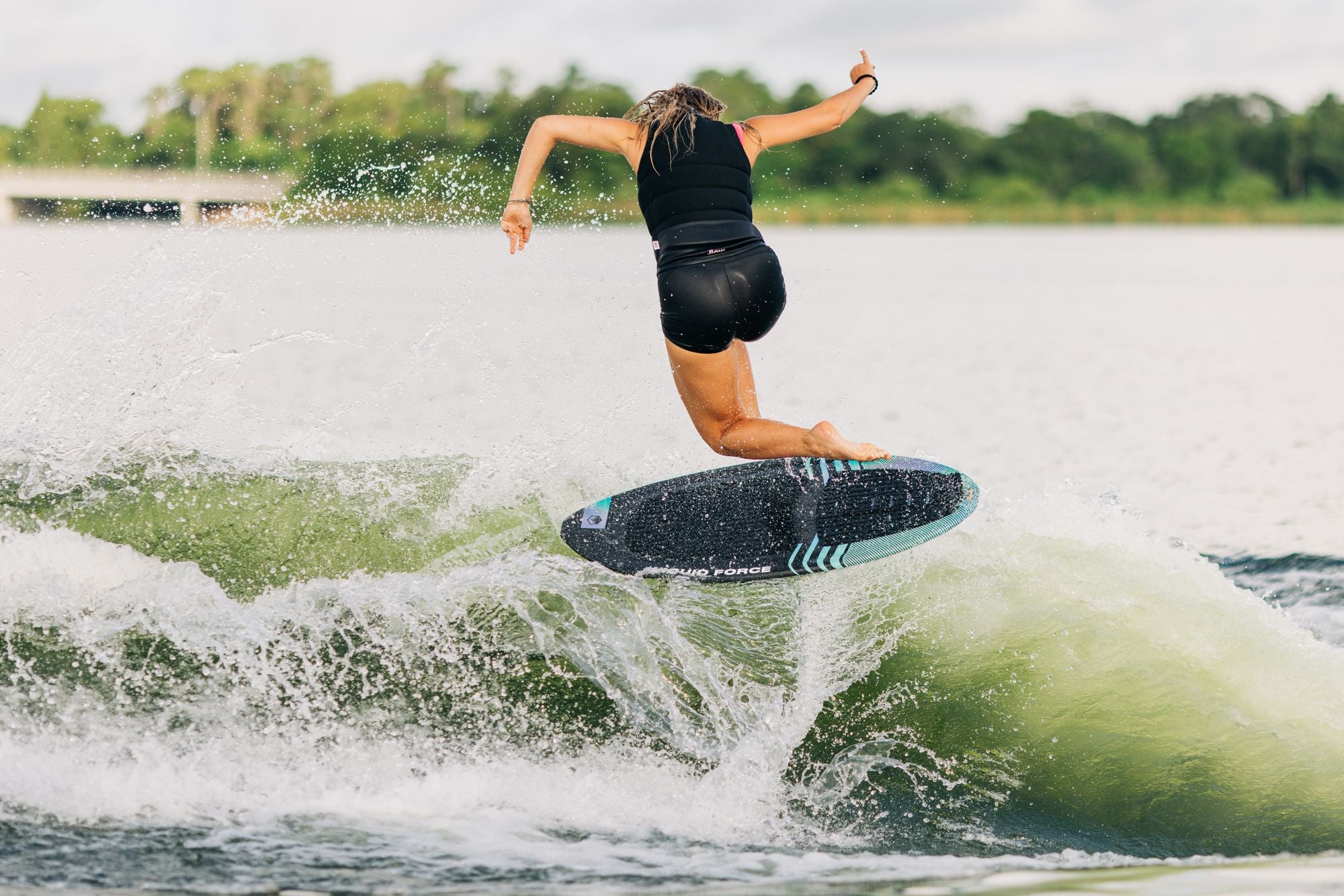 A lightweight woman is effortlessly gliding on a Liquid Force 2023 Neo Wakesurf Board, gracefully riding a wave like a skilled skim surfer.