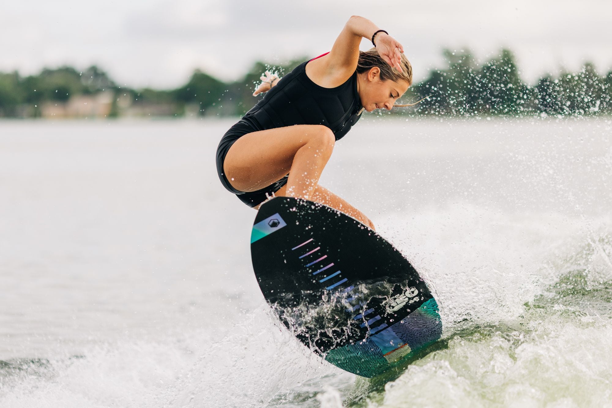 A Liquid Force 2023 Neo lightweight woman skim surfer gracefully riding a wakeboard on a serene lake.