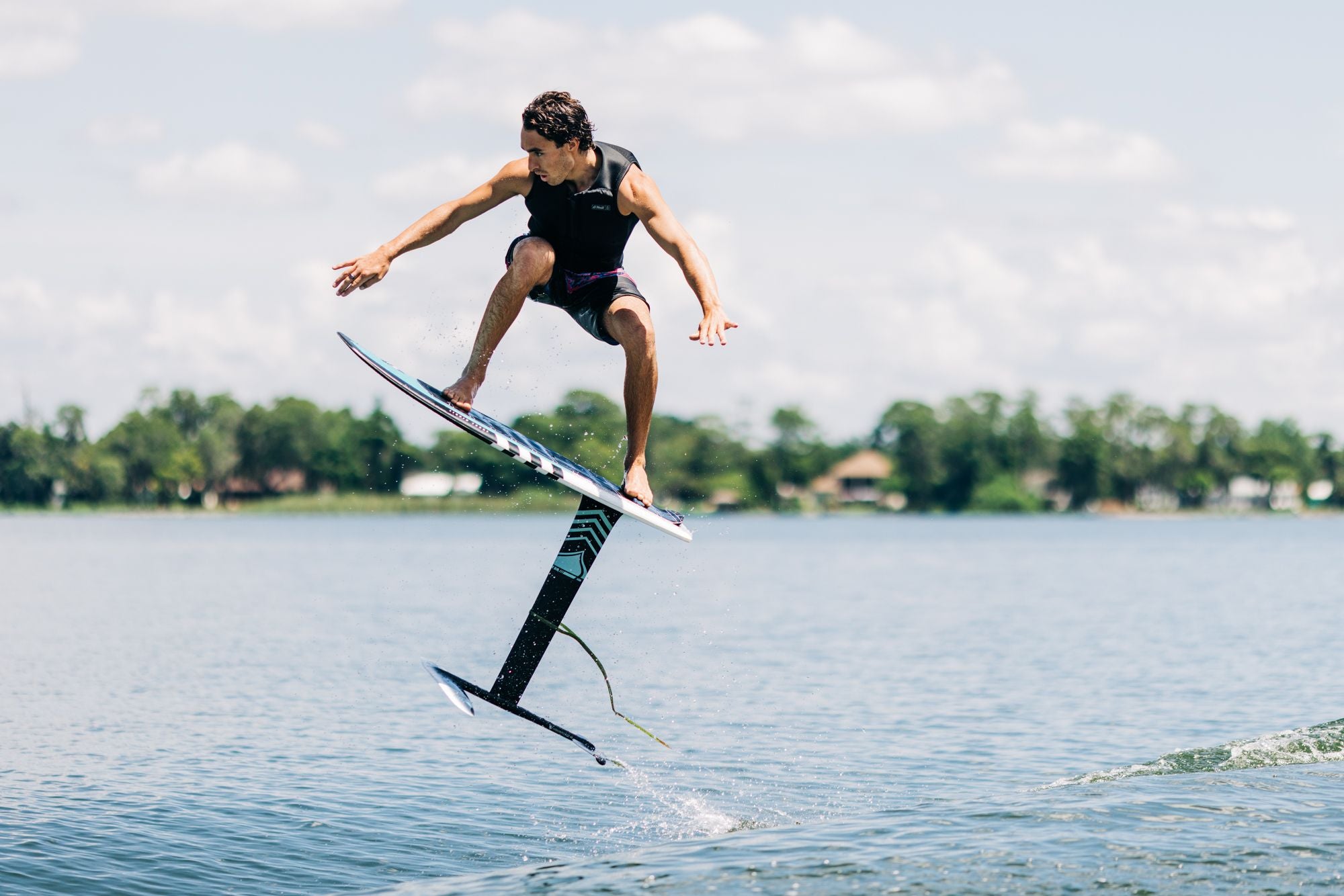 A man is wakesurfing on a Liquid Force 2024 Pod Foil Board on a lake.