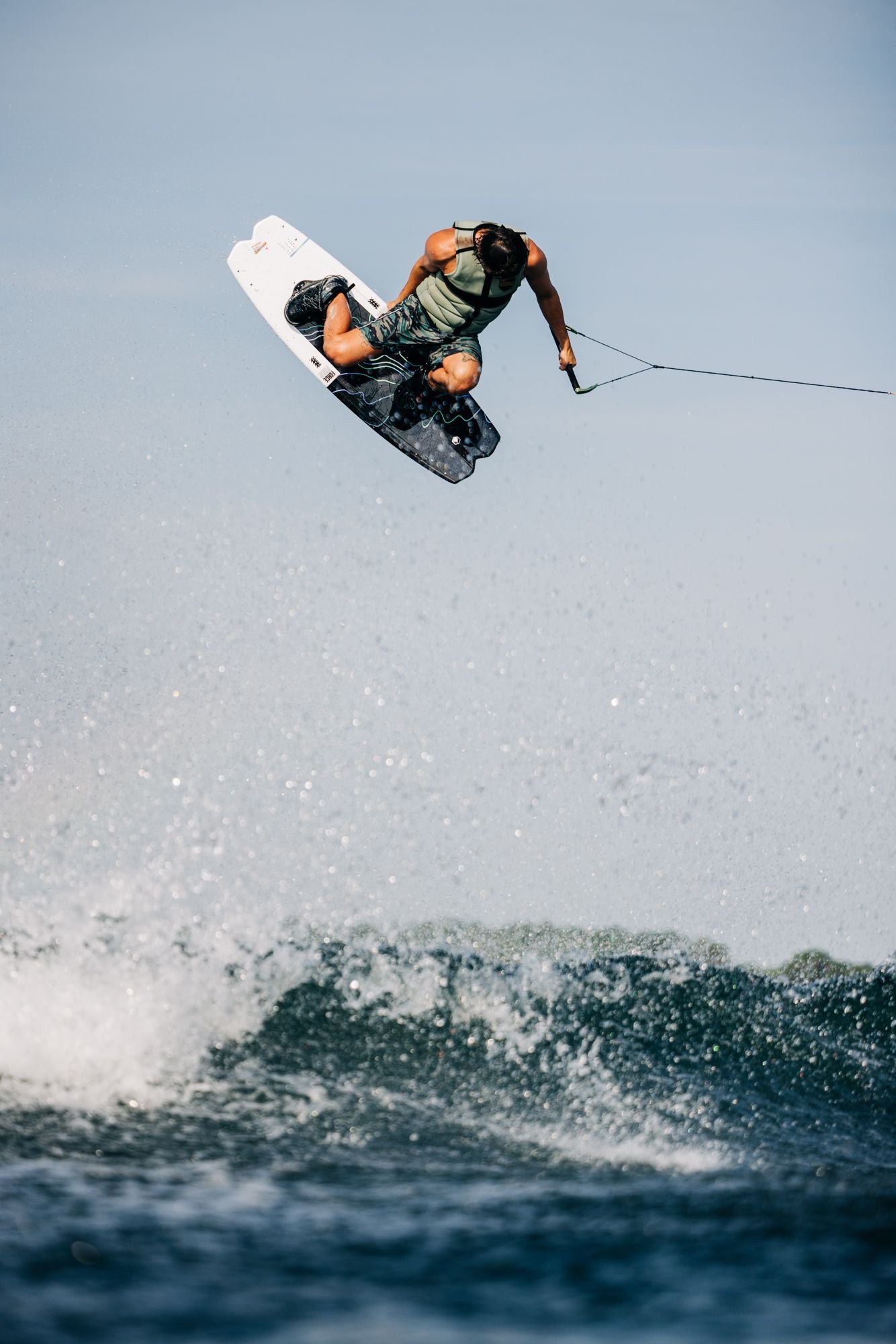 A man is riding a Liquid Force 2024 Remedy Wakeboard with a 3-Stage Rocker in the air.