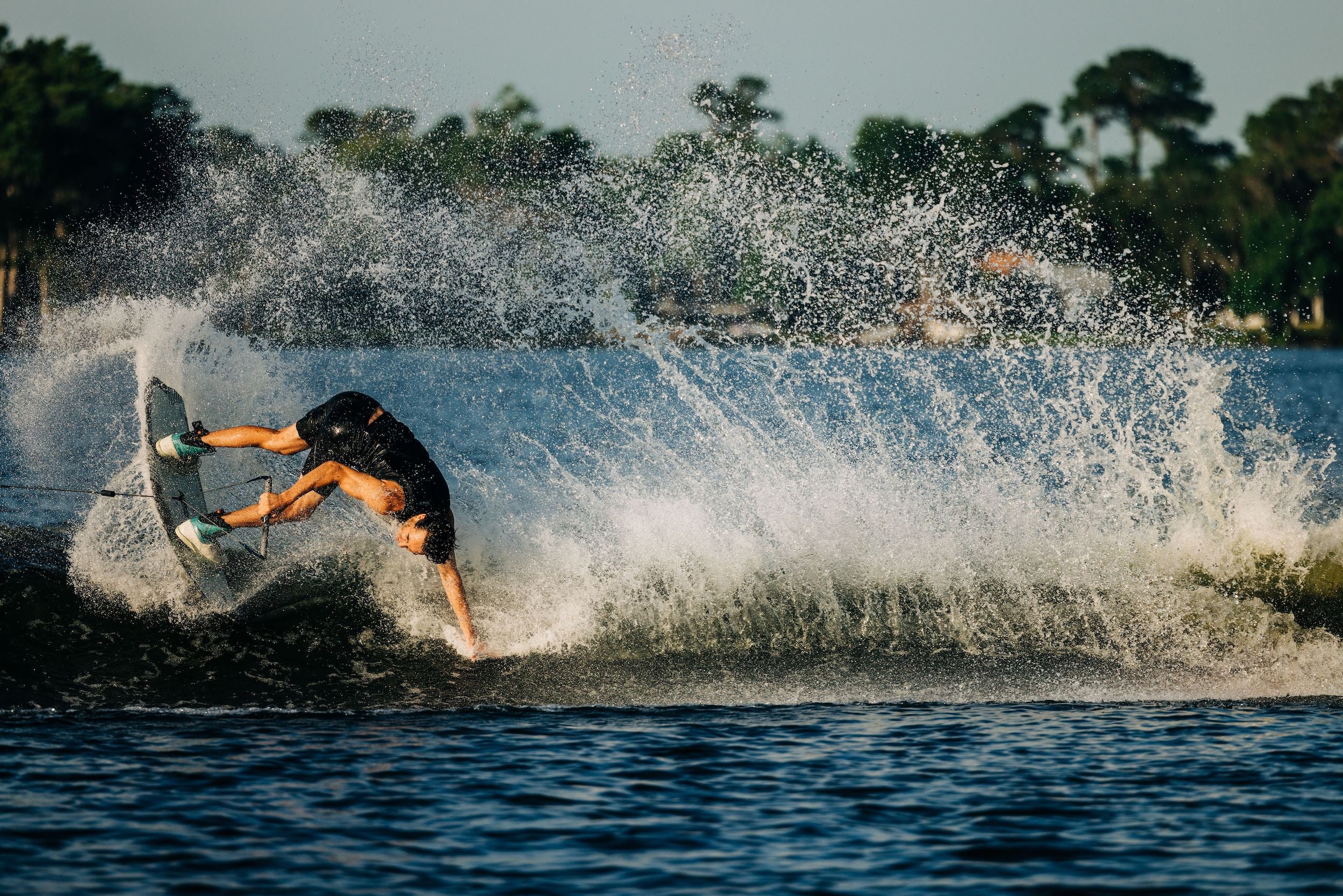 A person riding a Liquid Force 2023 Rhyme Wakeboard on a body of water, showcasing their skills as they navigate the waves with a boat board.