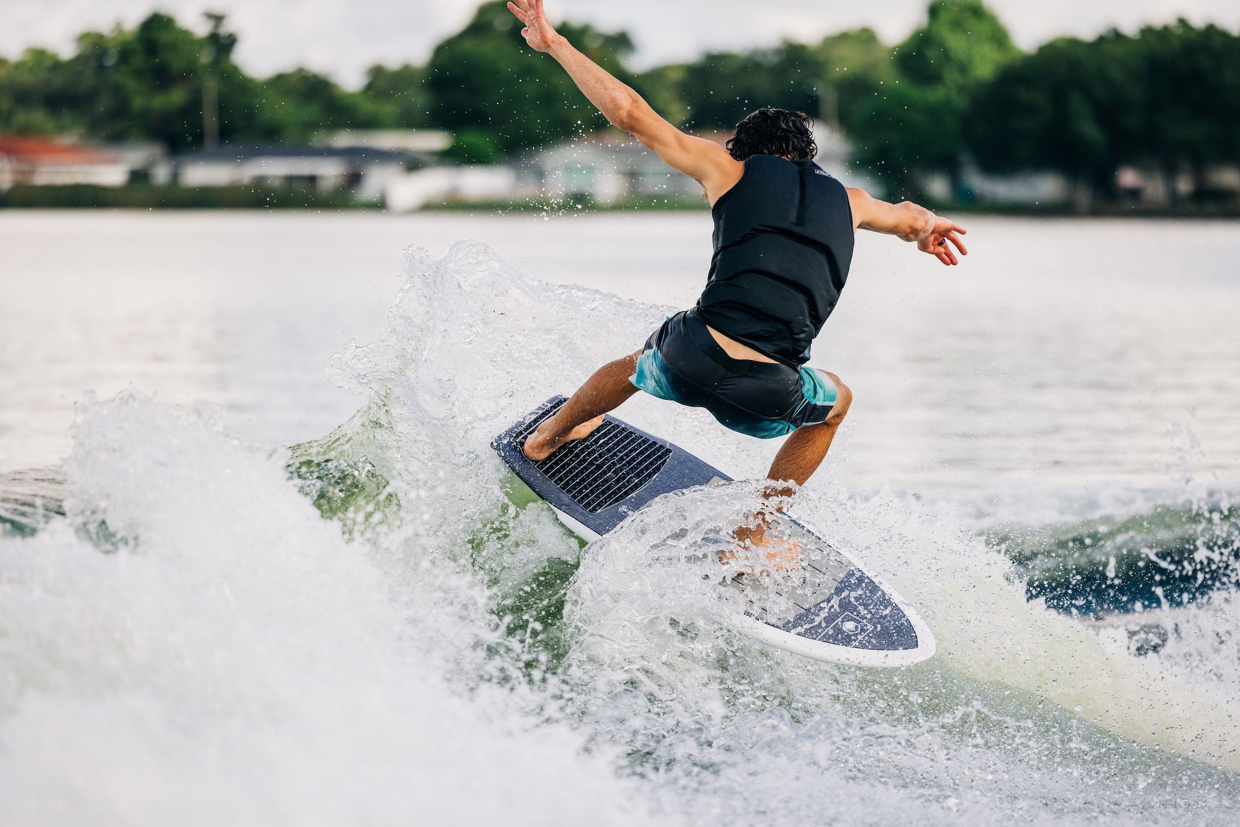 A man riding a Liquid Force 2023 Sting LTD Wakesurf Board on a lake.