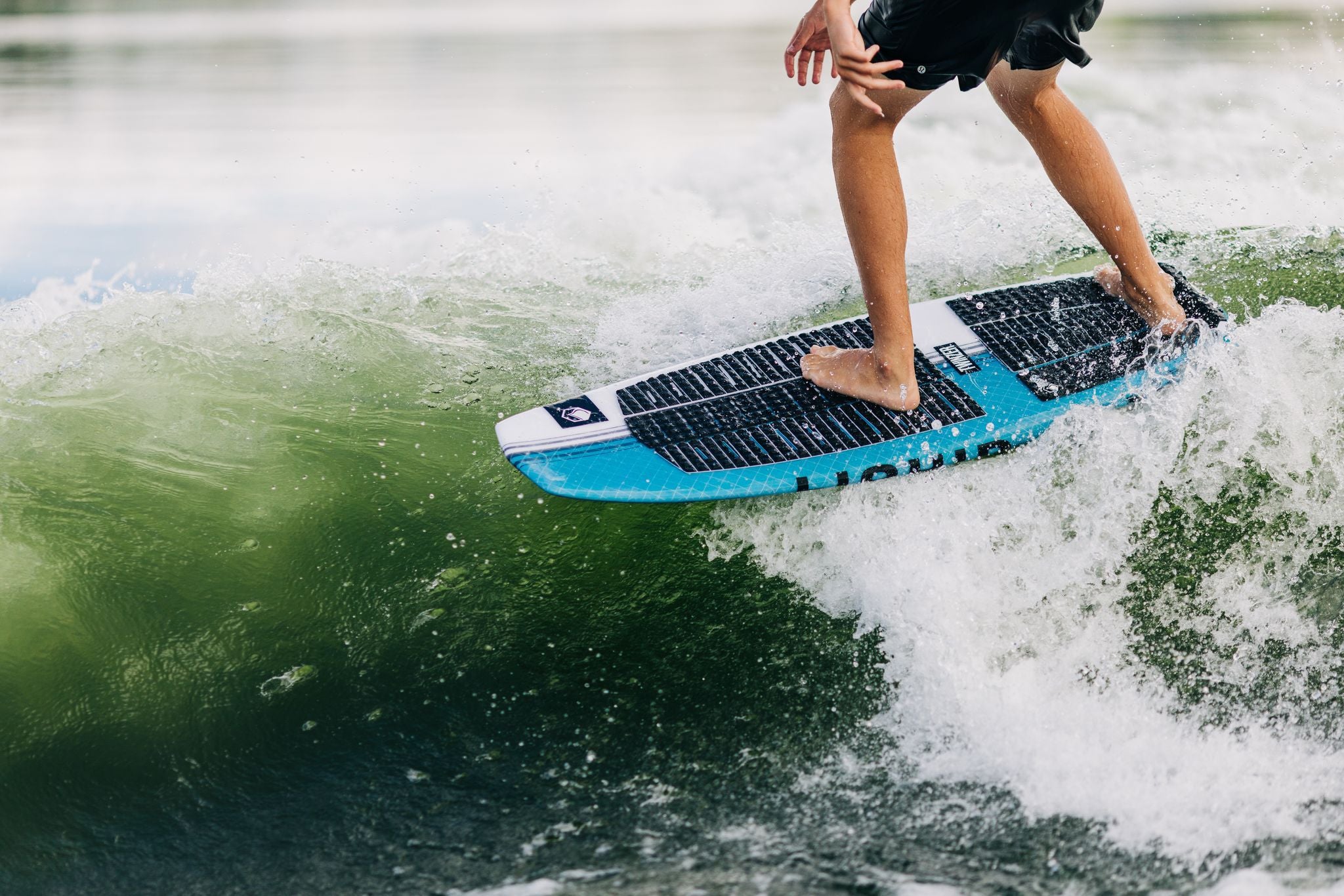 A person riding a surfboard, the Liquid Force 2024 Twinzer Wakesurf Board, with a Twinzer fin configuration on a concave wave.
