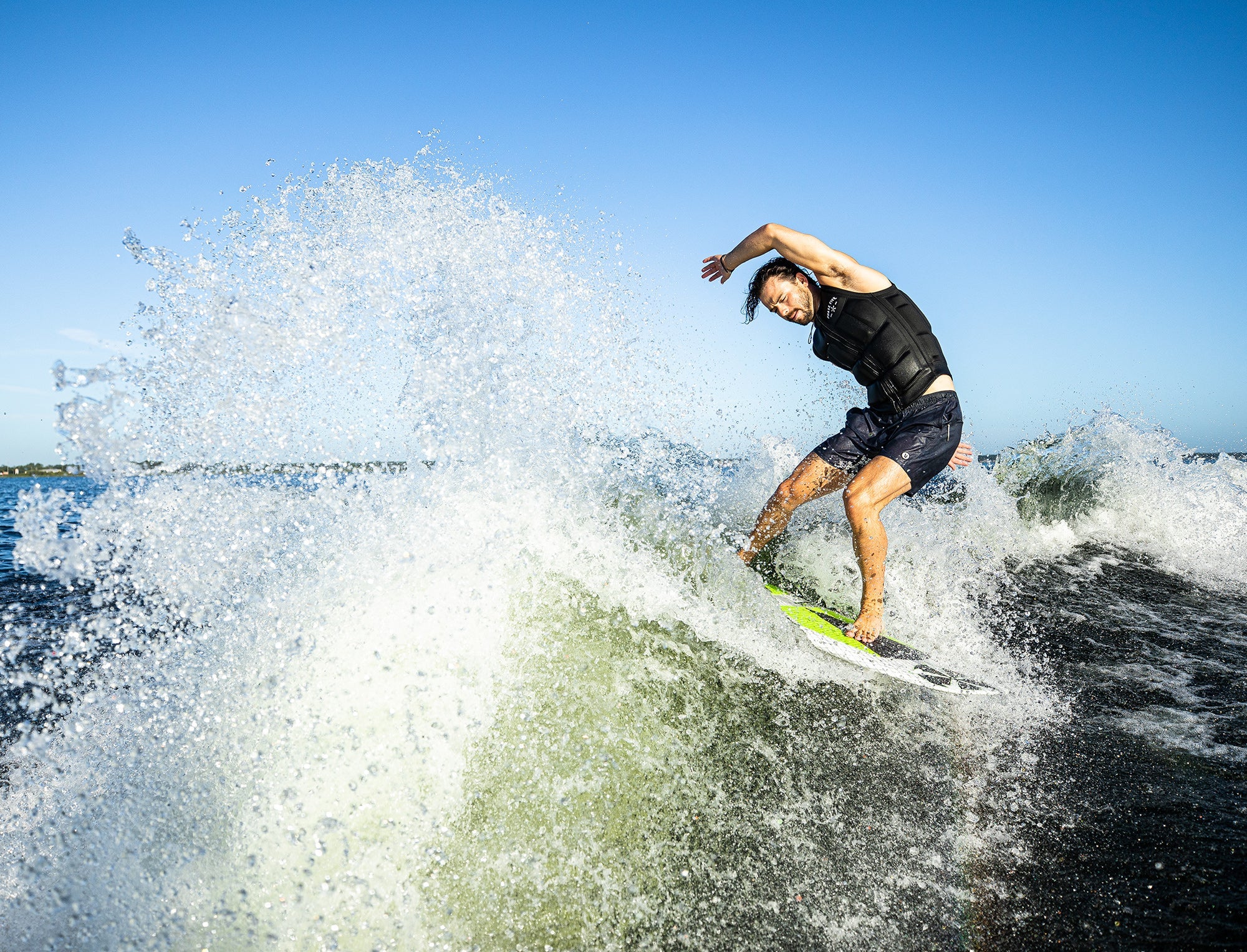 A Phase 5 2023 Doctor Wakesurf Board helps a big guy surfer ride a wave on his surfboard.