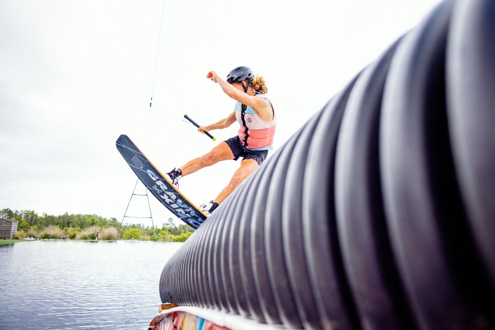 A woman is riding a wakeboard wearing a Ronix 2023 Coral Women's CE Impact Vest.